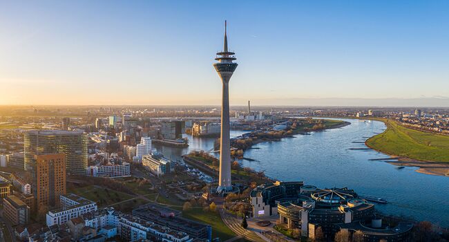 Stadtansicht von Düsseldorf mit dem Rheinturm und dem Rhein im Hintergrund, aufgenommen bei Sonnenuntergang.