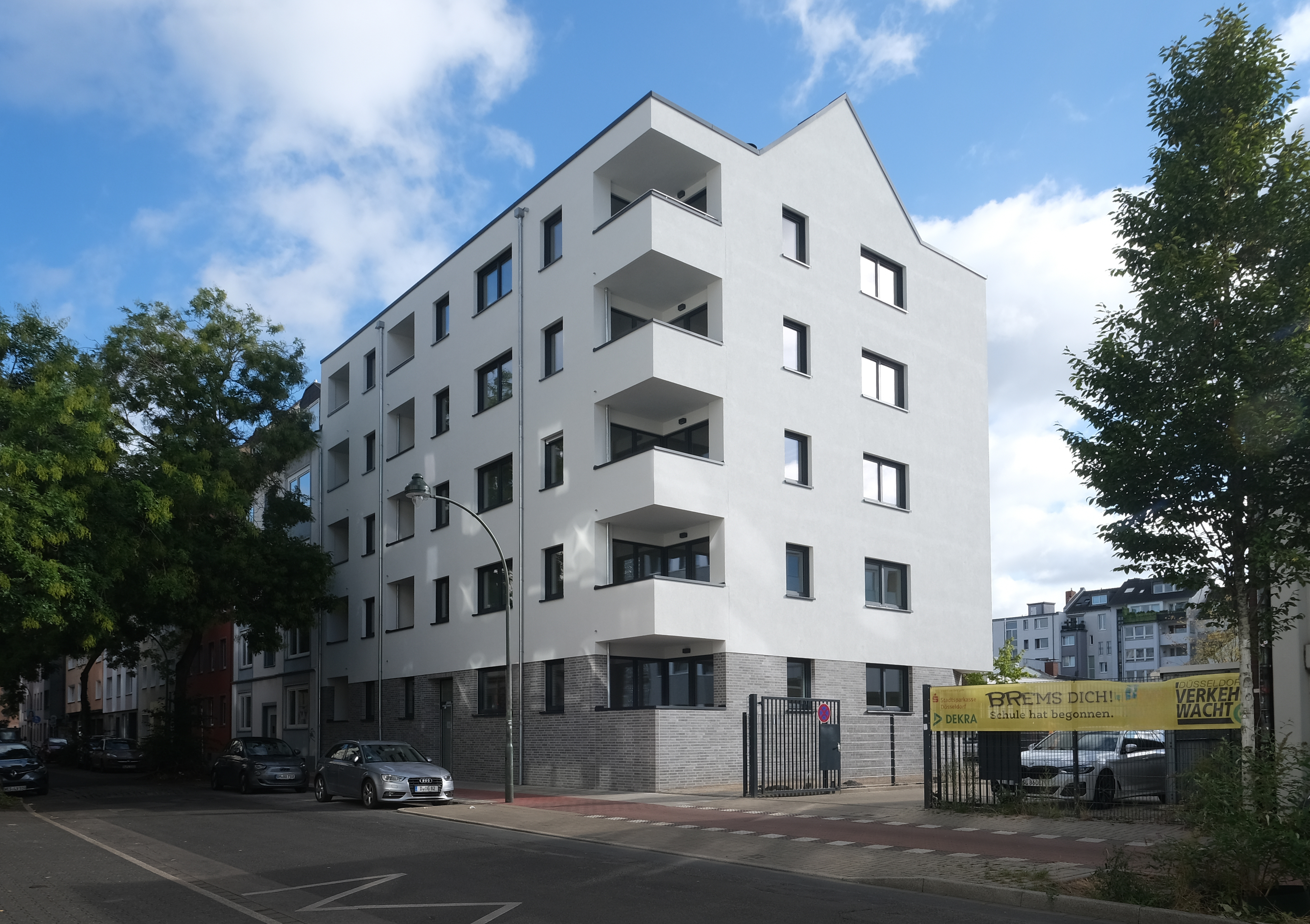 Architekturvisualisierung eines modernen mehrstöckigen Wohngebäudes in einer belebten städtischen Umgebung, charakterisiert durch seine klare weiße Fassade und geräumige Balkone, die das urbane Leben reflektieren.