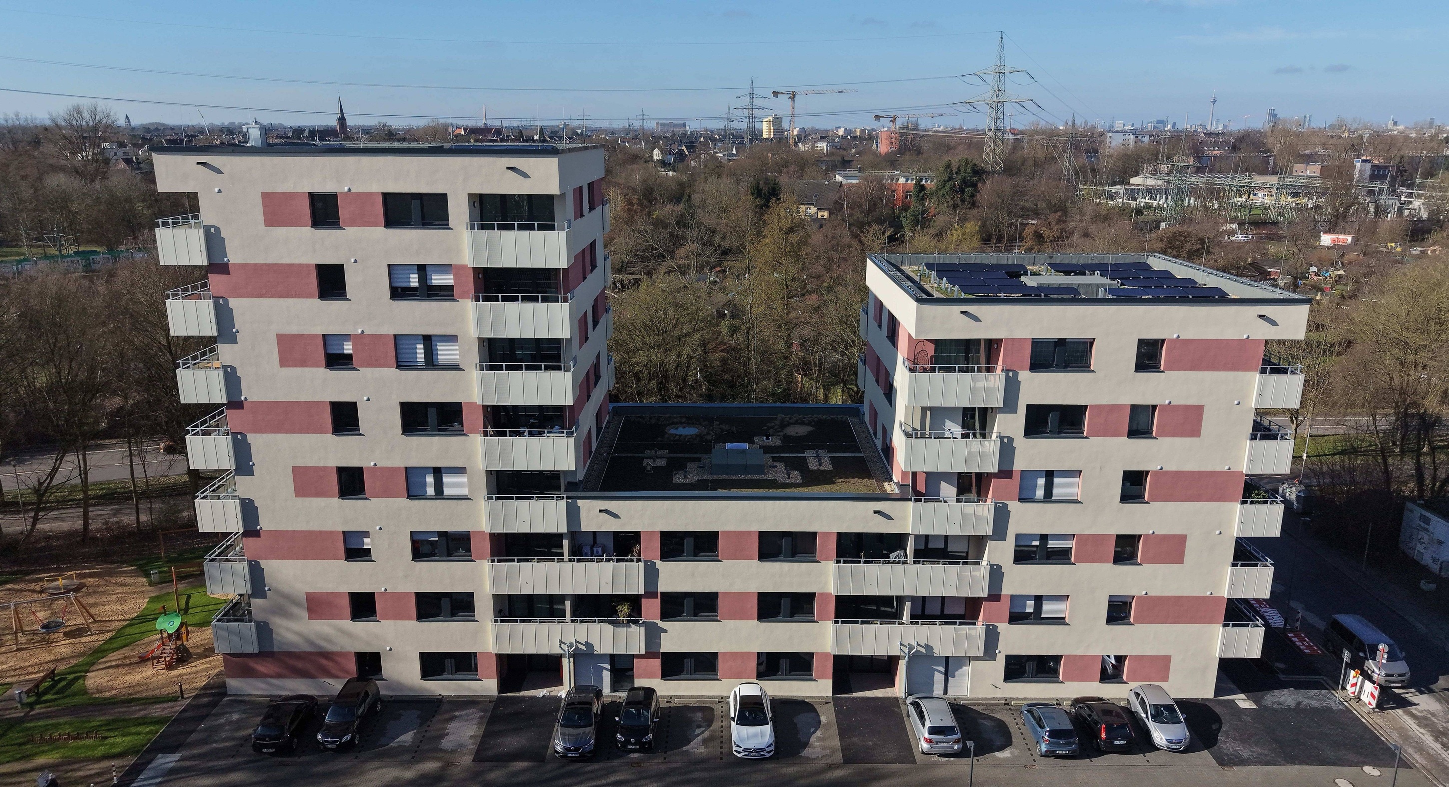 Ansicht eines modernen Wohngebäudes mit fünf Stockwerken, farblich in Beige und Burgund gehalten, in einer lebhaften städtischen Umgebung mit Passanten und Fahrradfahrern.